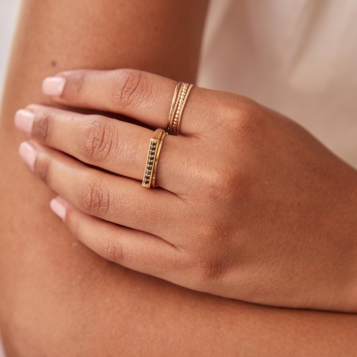 A hand wearing a Pave Geo Ring - Black Diamond, Flat Ring, Delicate Trio Stacking Rings and a Delicate Twist Band, all in yellow gold. 