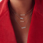 A close-up of a décolletage wearing a Pavé MAMA Necklace in rose gold, a Pavé Mrs Necklace in white gold, a Pavé MUM Necklace in yellow gold and a Pavé NANA Necklace in white gold, styled in a red corduroy jacket. 