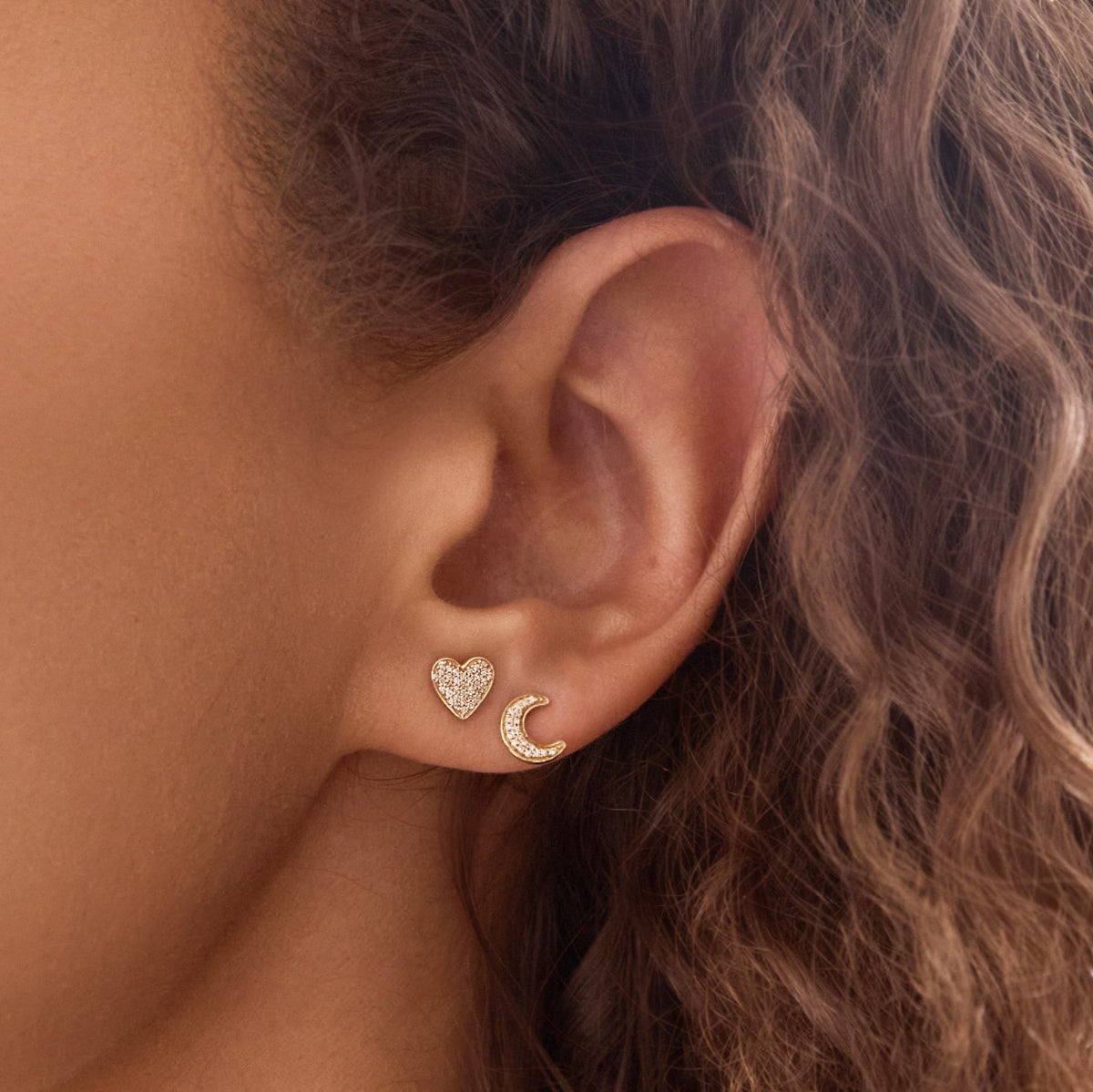 Close-up of an ear wearing a Pavé Charm Stud - Heart and a Pave Charm Stud - Moon in yellow gold. 