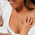 Close-up of a woman's neck wearing a yellow gold Custom Gold Necklace — 2 Letters (S and a heart charm) and a white gold Pavé MADRE Necklace, in a white T-shirt, smiling and holding a child.