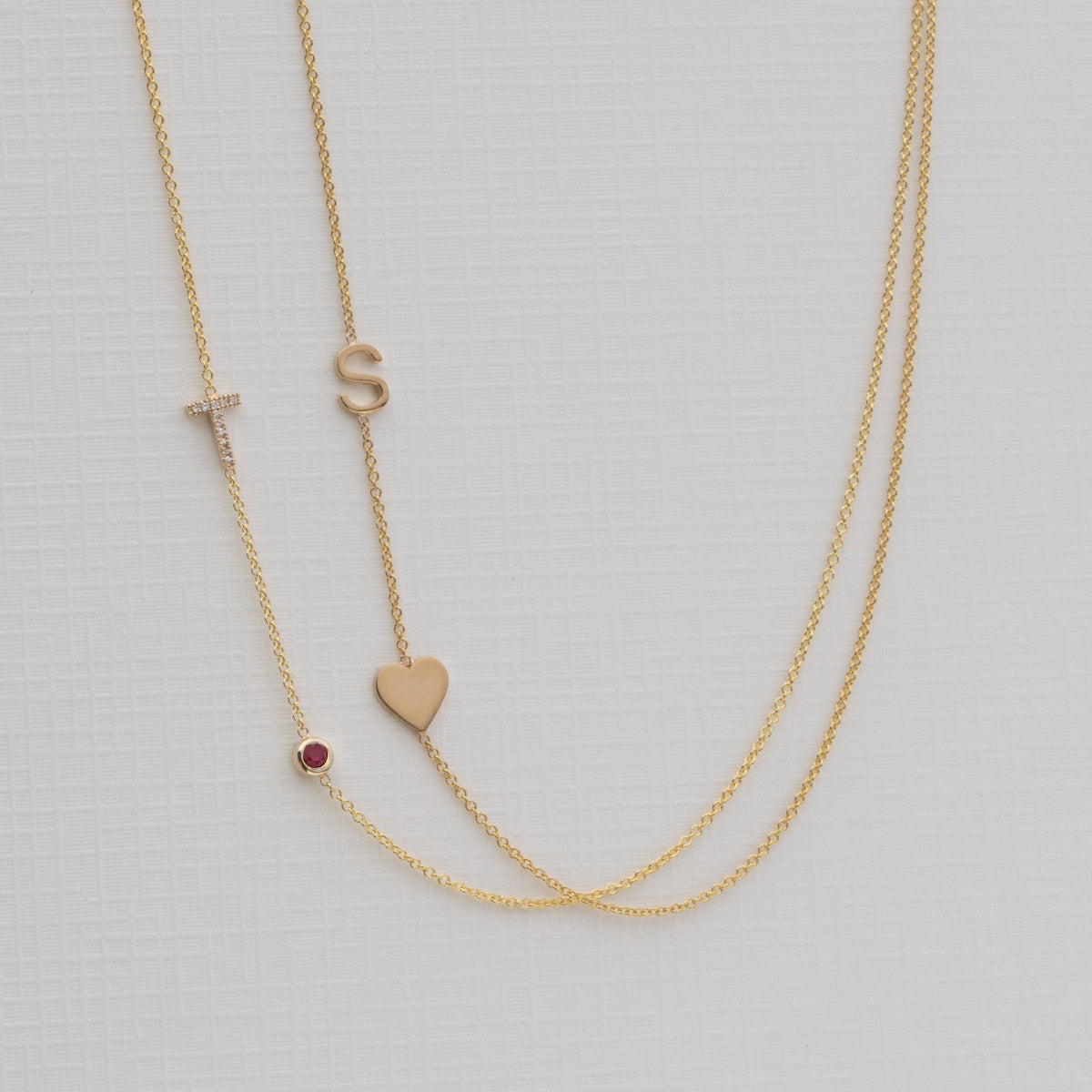 Gold necklace with small heart and letter 'S' pendant on a light gray background