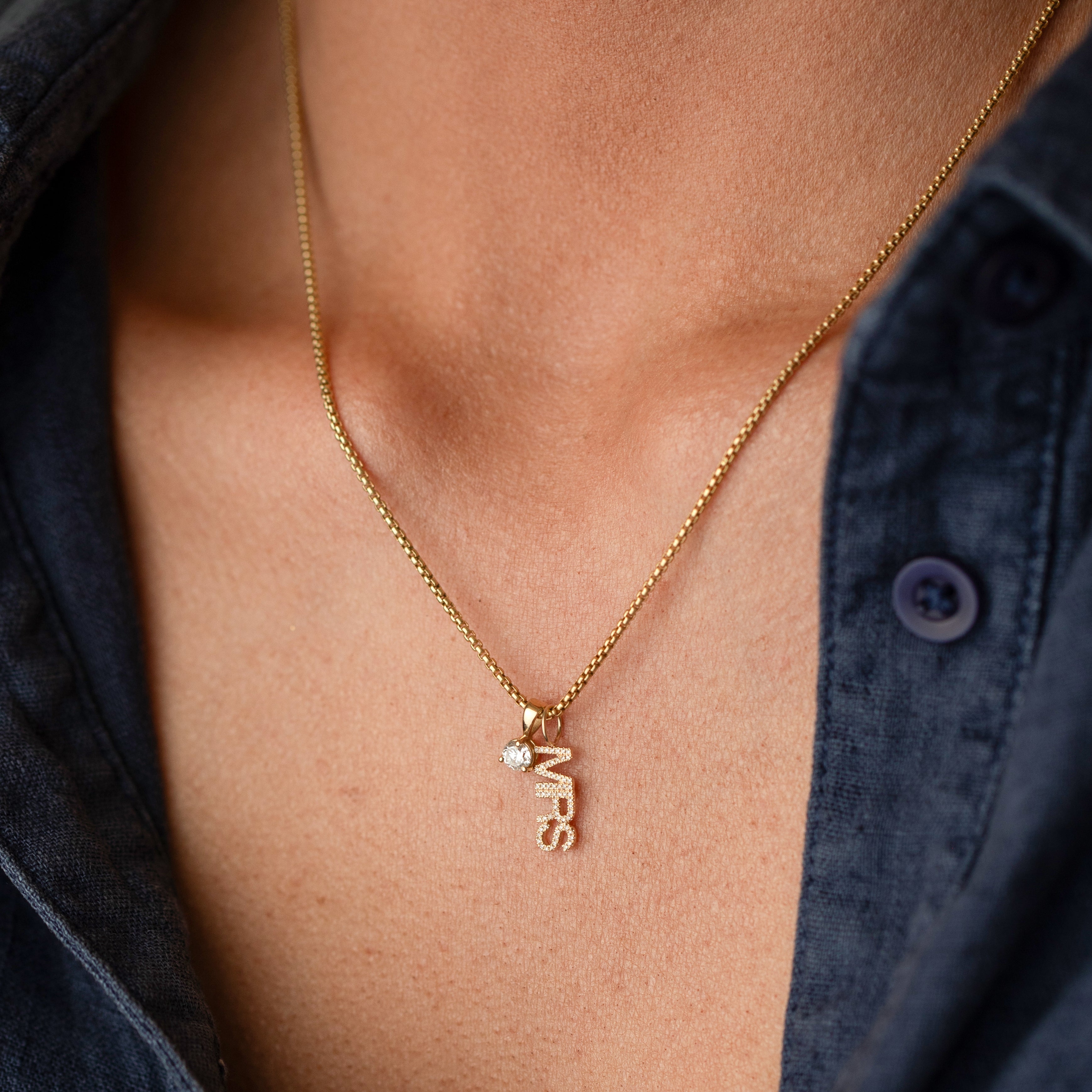 Gold necklace with a 'MRS' pendant on a person wearing a dark blue shirt.