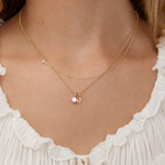 Necklace with a small gold letter pendant worn by a person in a white dress