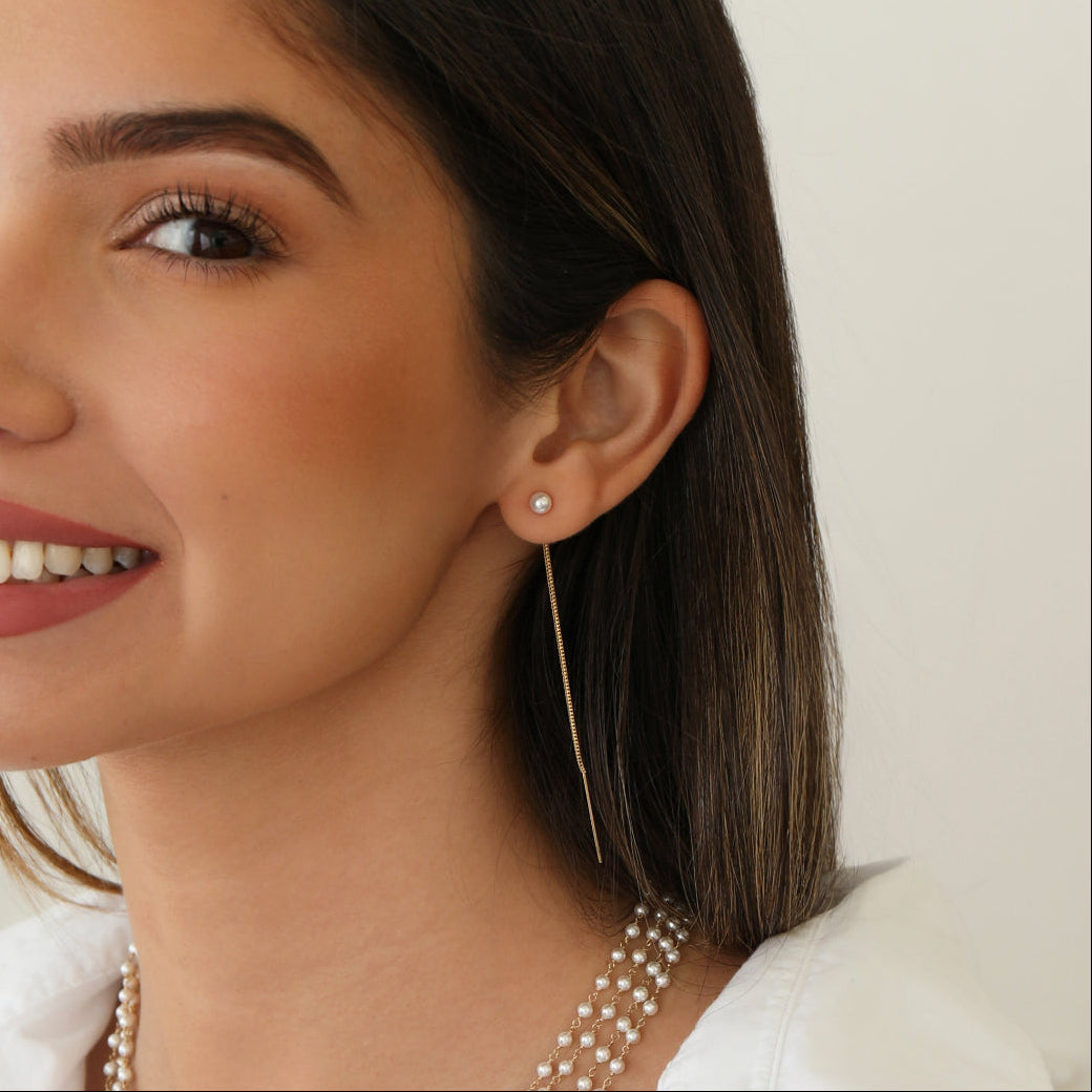 A woman wearing a Pearl Drift Threader, several The Lily Bouquet Necklaces and a white top, with brown hair against a neutral background.