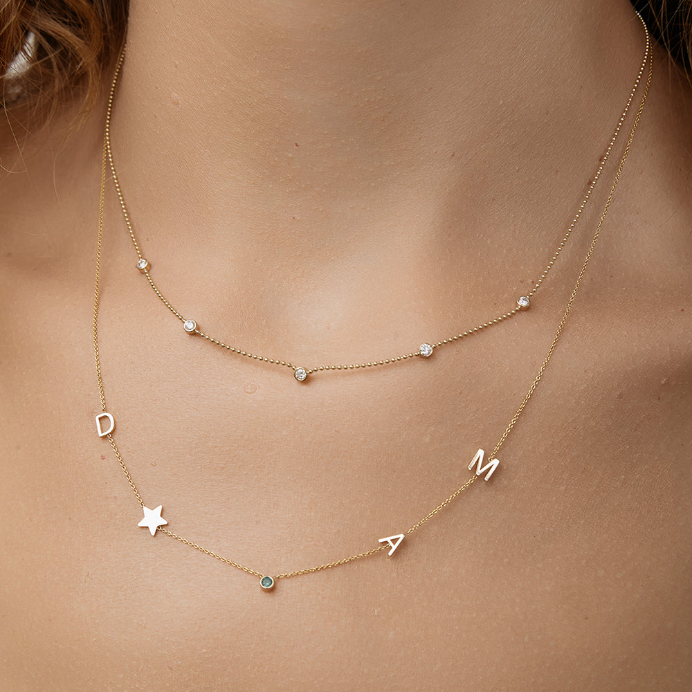 Quintet Diamond Necklace layered with Gold initial necklace on a person's neck.