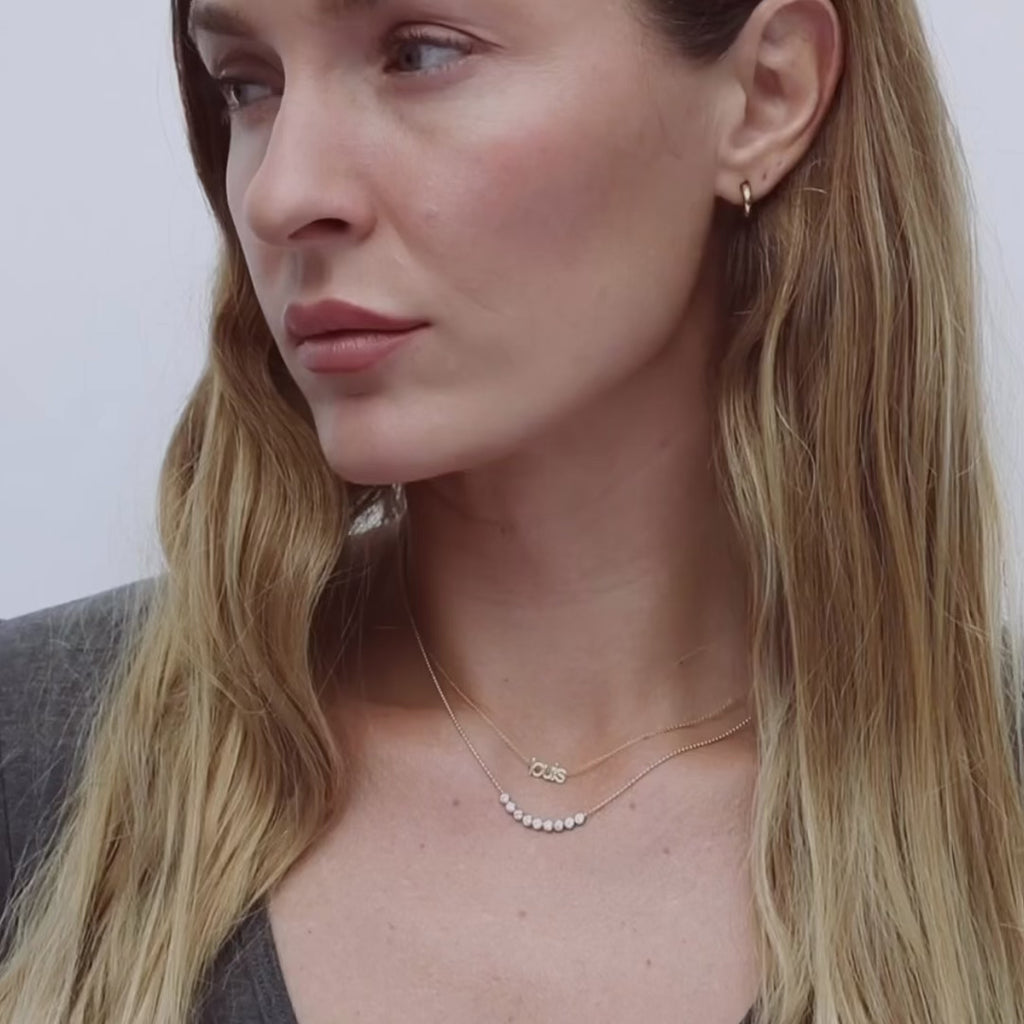 video of woman wearing diamond arc and petit nameplate necklace in yellow gold on white background