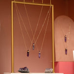 Several The Healing Retreat Necklaces on gold and pink stands with amethyst crystals against a light brown background. 