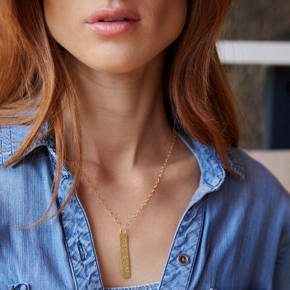 Close-up of a woman's neck wearing a Virtues Pendant - Rectangle in yellow gold with a blue denim shirt. 