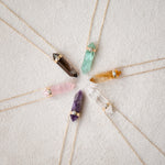 Five Retreat Necklaces (Courage, In Flow, Happiness, Clarity, Healing and Love) on a cream carpet background. 
