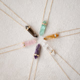 Five Retreat Necklaces (Courage, In Flow, Happiness, Clarity, Healing and Love) on a cream carpet background. 