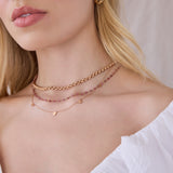 Close-up of a blonde woman's neck wearing a rose gold Rolo Necklace, the Peony Bouquet Necklace and a 5 of Hearts Necklace, with a white top against a neutral background.