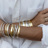 Close-up of arms wearing silver and god Rendezvous Cuffs, Plus One Cuffs and All In Cuffs, a C'est Moi Link Ring and an Open Diamond Ring,  styled with a white shirt. 