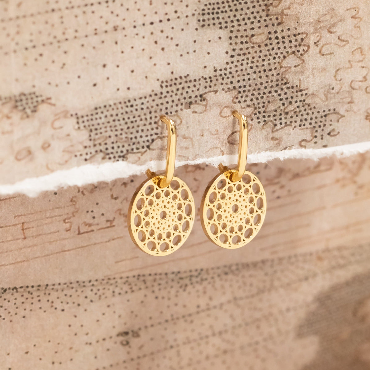 Gold Skylight Hoops on a textured beige surface.
