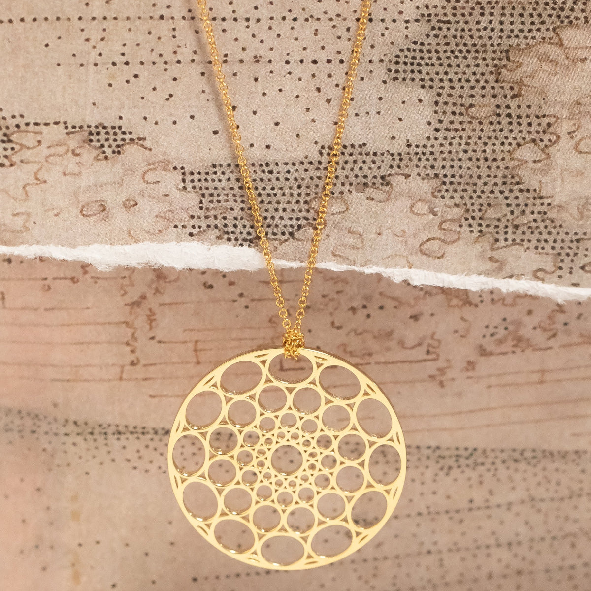 A Skylight Necklace in yellow gold against a textured beige background. 