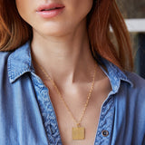 Close-up of a woman's neck wearing a Virtues Pendant - Square in yellow gold with a blue denim shirt against a blurred background. 