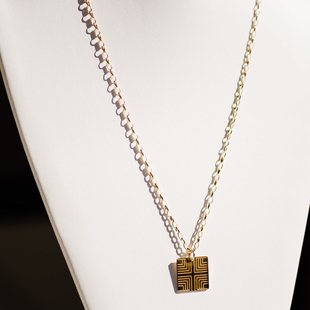 A Virtues Pendant - Square in yellow gold on a white necklace stand. 