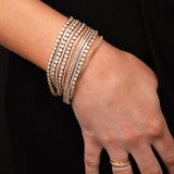 A hand wearing several white gold and yellow gold Love Set Match Bracelets and Down the Line Bracelets, and several yellow gold rings against black background. 