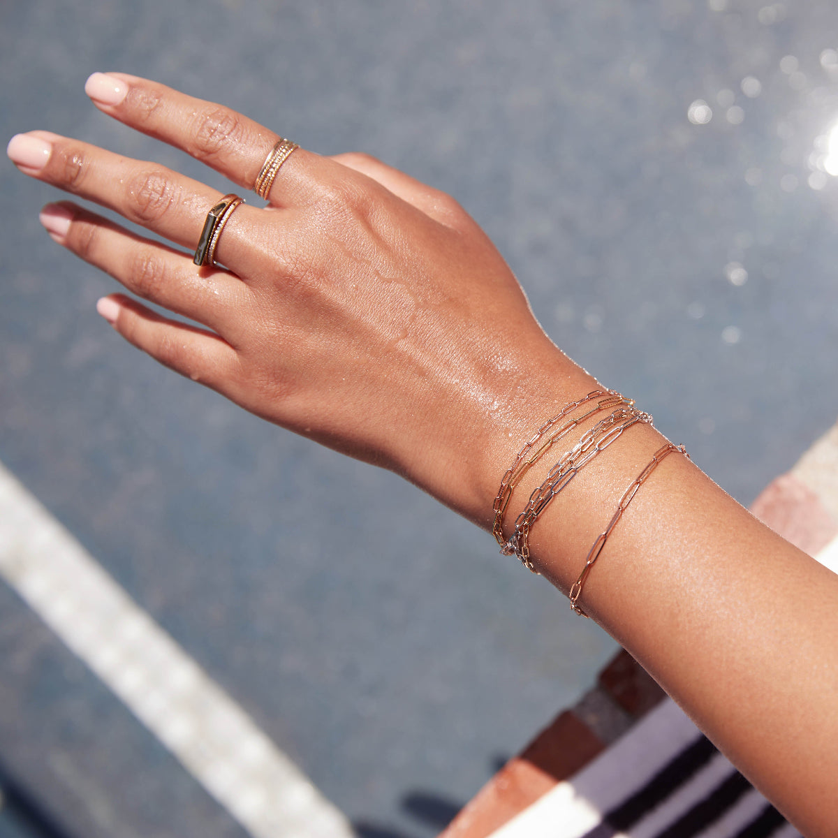 A hand wearing several stacked Element Short Link Bracelets and Element Long Link Bracelets, Delicate Trio Stacking Rings, a Geo Stacking Ring and a Pavé Diamond Ring.