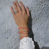 A hand wearing a Perla Pinky Ring, Tres Pearl Ring, an Open Diamond Ring, a Tenfold Ring and an Endless Summer Necklace - Calypso and an Endless Summer Bracelet - Mykonos with a light stone background. 