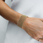 A close-up of a woman's wearing multiple Classic Beaded Bracelets stacked, with a white top. 