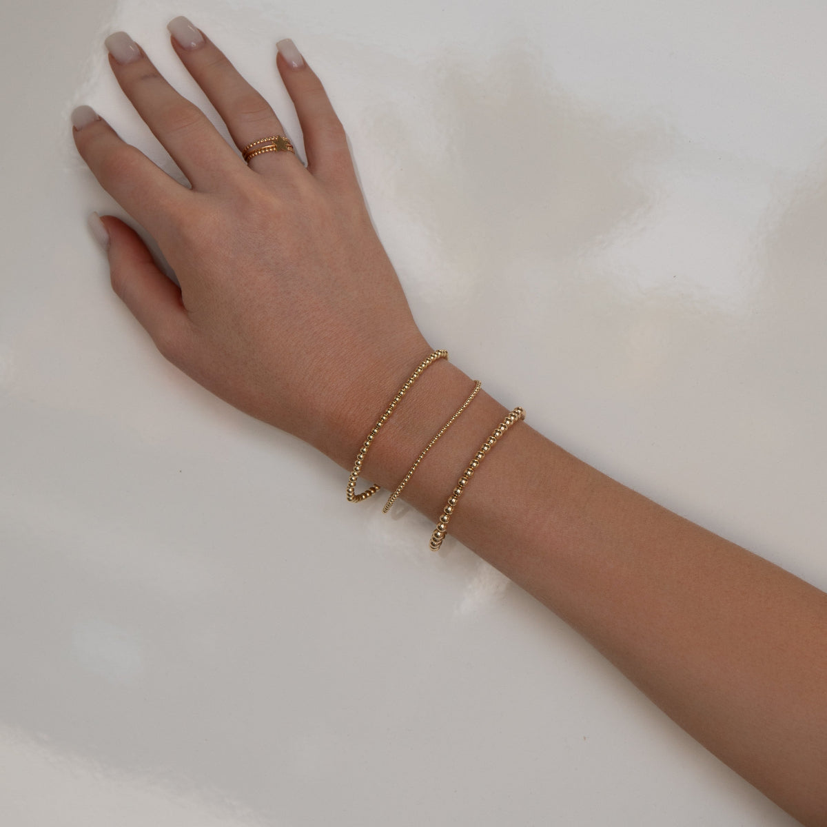 A hand wearing a Classic Bubble Bracelet Set, two Delicate Beaded Bands and a Twinkle Twinkle ring against a neutral background.