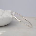 A sterling silver Flirt Bangle against a light marble bowl and a light grey surface. 