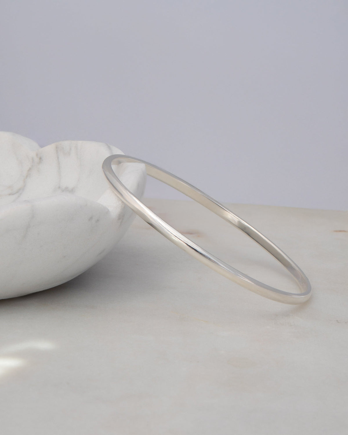 A sterling silver Flirt Bangle against a light marble bowl and a light grey surface. 
