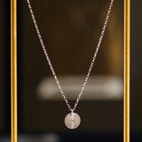 A Virtues Pendant - Circle in sterling silver  in a thin gold frame and a blurred background. 