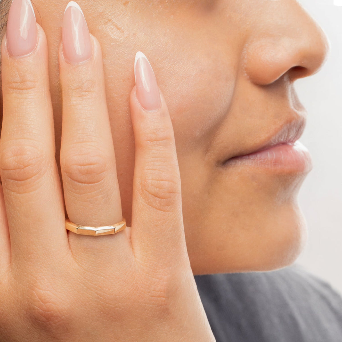 Close-up of a woman's hand wearing a yellow gold Tenfold Ring placed on her face, with a blurred background. 