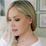 A Thin Gold Hoop, Lip Stud and an Element Long Link Chain in yellow gold worn by a blonde woman against a blurred background. 