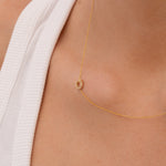 Gold necklace with a small pavé diamond horseshoe charm  on a person's neck with a blurred background