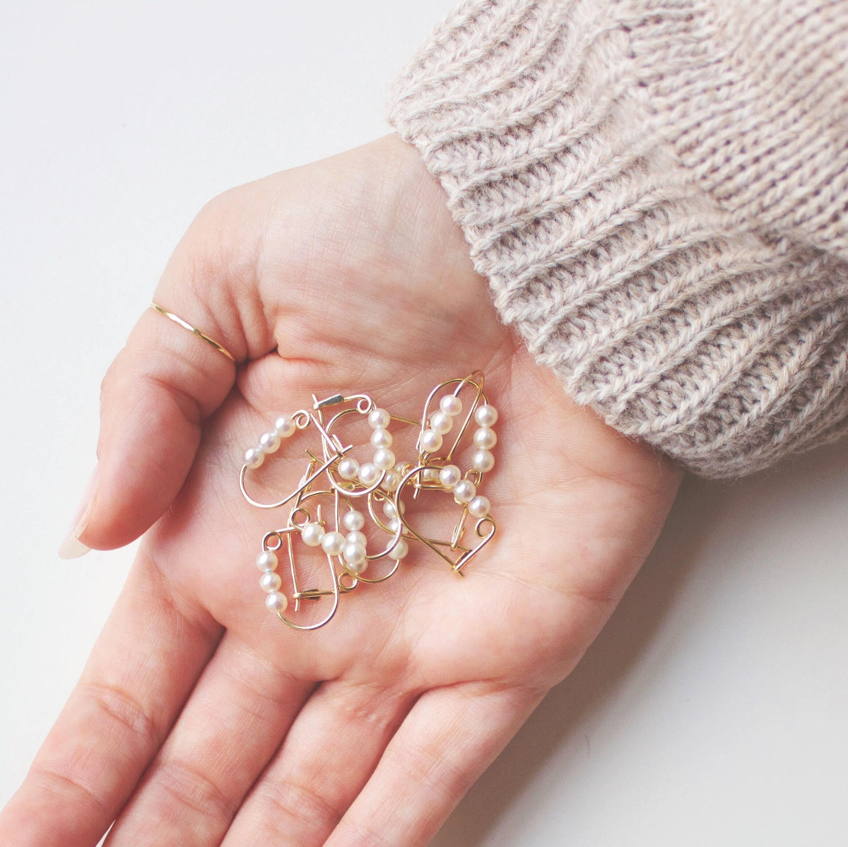 A hand holding several Tres Pearl Earrings in against a white background. 