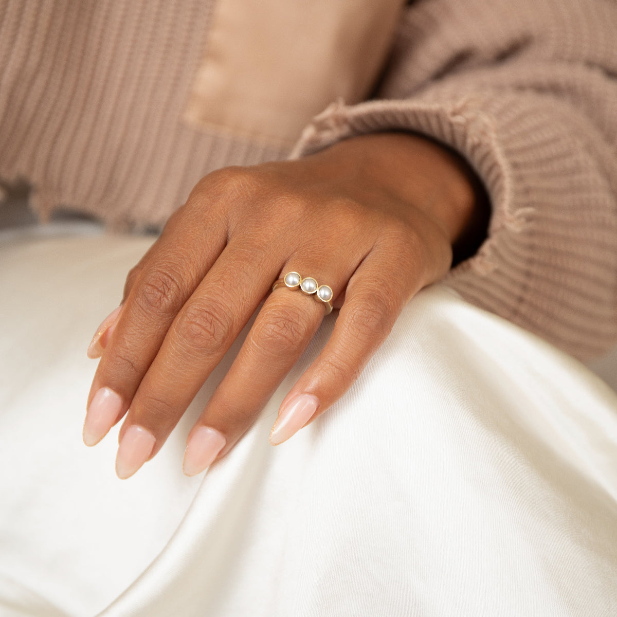 A woman's hand wearing a Tres Pearl Ring resting on her white pants in a neutral top. 