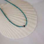 An Endless Summer Necklace - Santorini laid on a white shell against a white fabric background. 