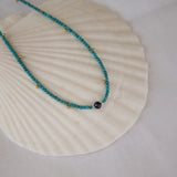 An Endless Summer Necklace - Santorini laid on a white shell against a white fabric background. 