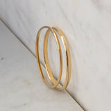 A vermeil gold Flirt Bangle and For Keeps Bangle on a light marble surface. 