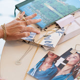 Virtues Pendants - Circle and Square in sterling silver laid out with images and books on a table, alongside a hand wearing a Perla Pinky Ring, Paris Ring, Link Ring and several bracelets, including a Rolo Bracelet and a Love Set Match Bracelet.