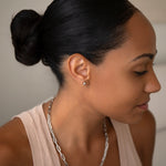 A woman wearing a white gold Preppy Post and a Bold Link Chain with a nude tank top and her black hair in a bun, against a light grey background.