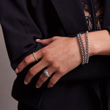 A close-up of a woman’s hand wearing three Rolo Bracelets, an Evermore Ring and an Etched Paris Ring, all in white gold, with a navy suit and lace top.