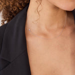 Close-up of a person wearing a delicate necklace with a small cross charm in white gold.