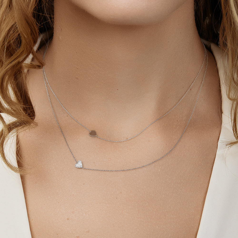 Close-up of a person wearing two delicate necklaces with heart charms layered together.