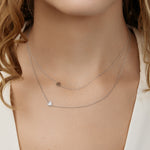 Close-up of a person wearing two delicate necklaces with heart charms layered together.