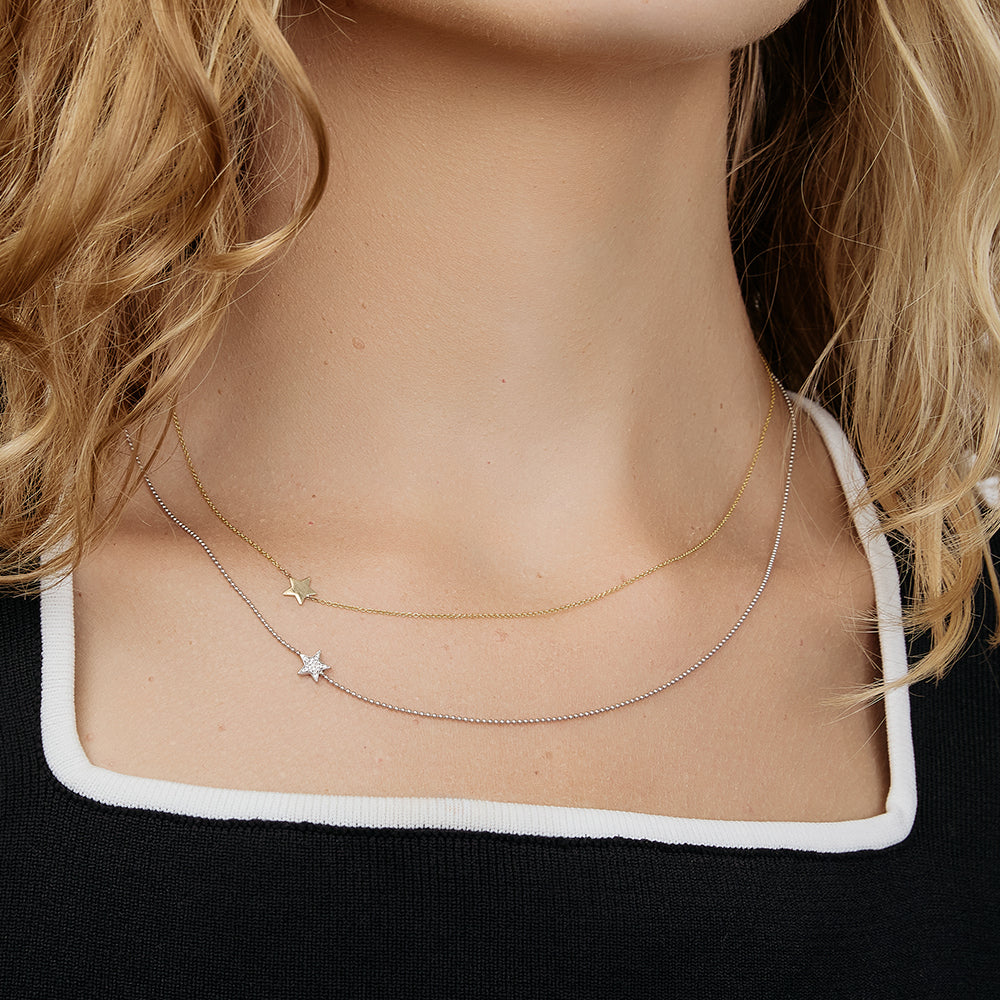 Close-up of a person wearing two gold necklaces with star charms.