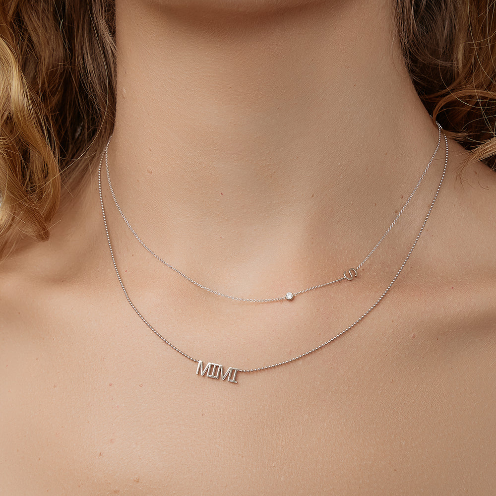 White Gold initial necklace with a diamond layered with a 'MIMI' wordplate necklace on model's neck.