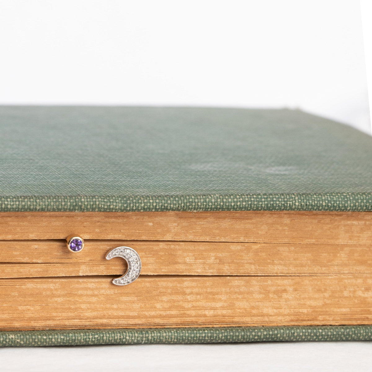 A white gold Pavé Charm Stud - Moon and Birthstone Stud - Amethyst  in a book against a white background. 
