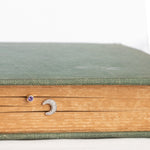 A white gold Pavé Charm Stud - Moon and Birthstone Stud - Amethyst  in a book against a white background. 