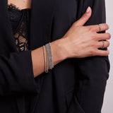 A close-up of a woman’s arm and hand wearing five Diamond Cut Bracelets, a Heartfelt Ring and an Evermore Ring, all in white gold, with a navy jacket and lace top.