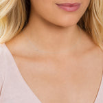 A close-up of a woman's neck wearing a white gold necklace with a letter T charm. 
