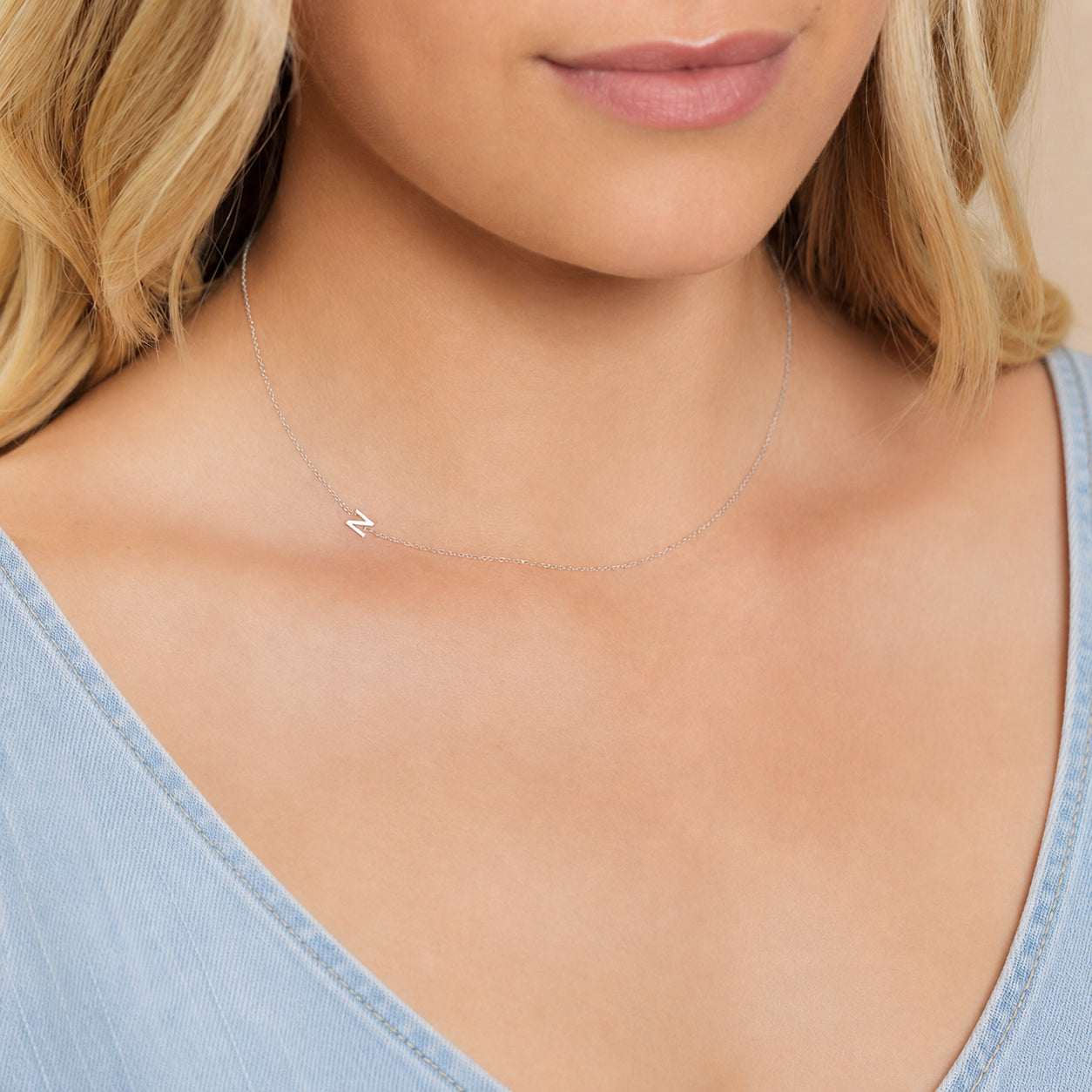 Close-up of a woman's neck wearing a white gold necklace with a letter N charm. 