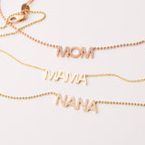 A Pavé MOM Necklace in rose gold, a MAMA Necklace in yellow gold and a  Pavé MOM Necklace in yellow gold, on an off-white background. 